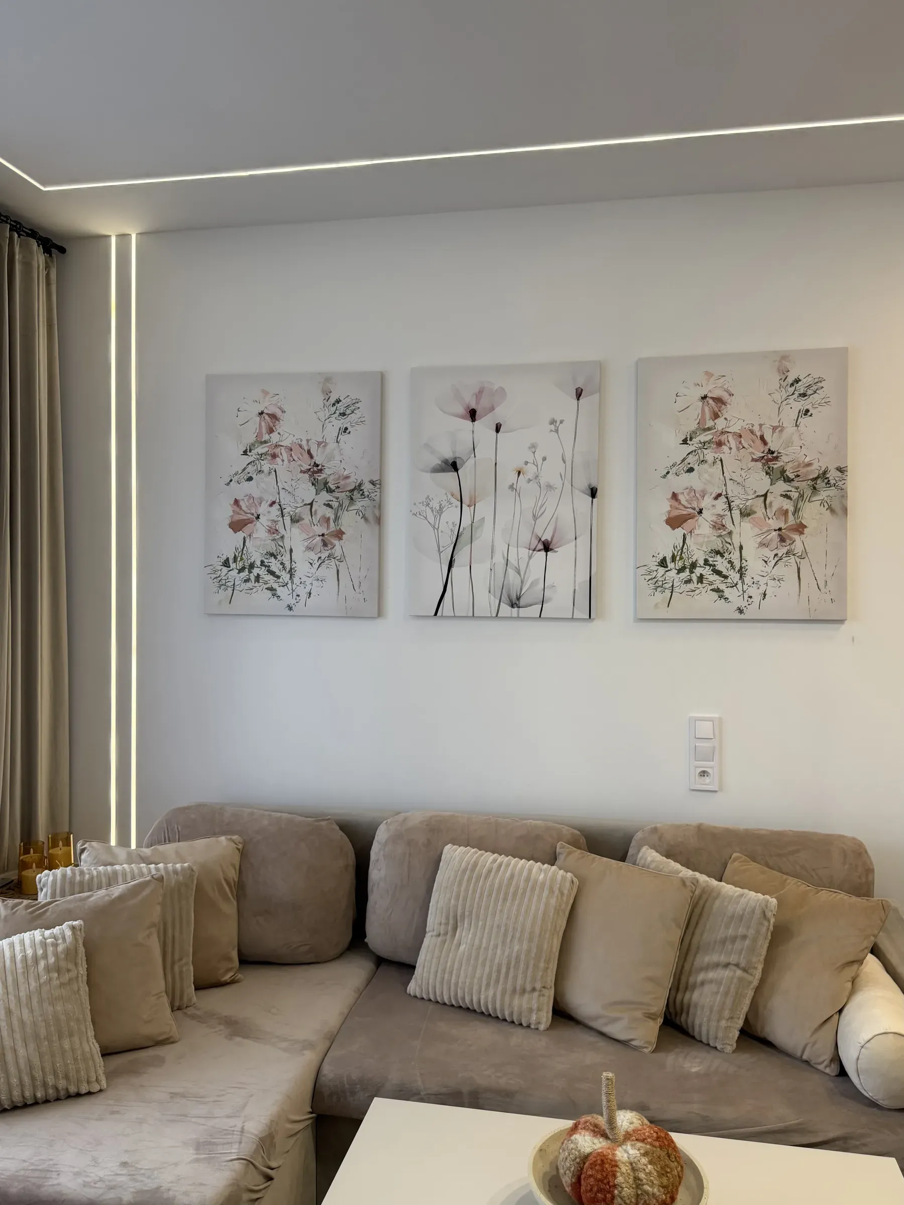 Sofa narożna z poduszkami i tryptyk kwiatowy na ścianie salonu